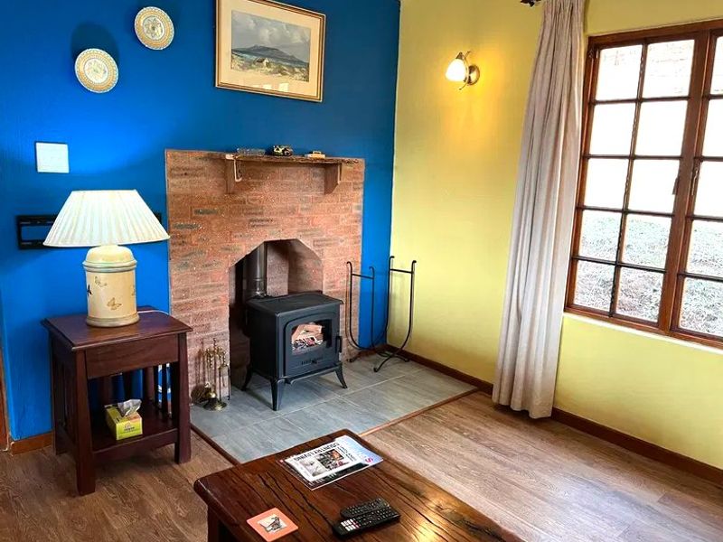 A cozy living room featuring a prominent brick fireplace with a wood-burning stove, timber-framed windows, and laminate flooring.