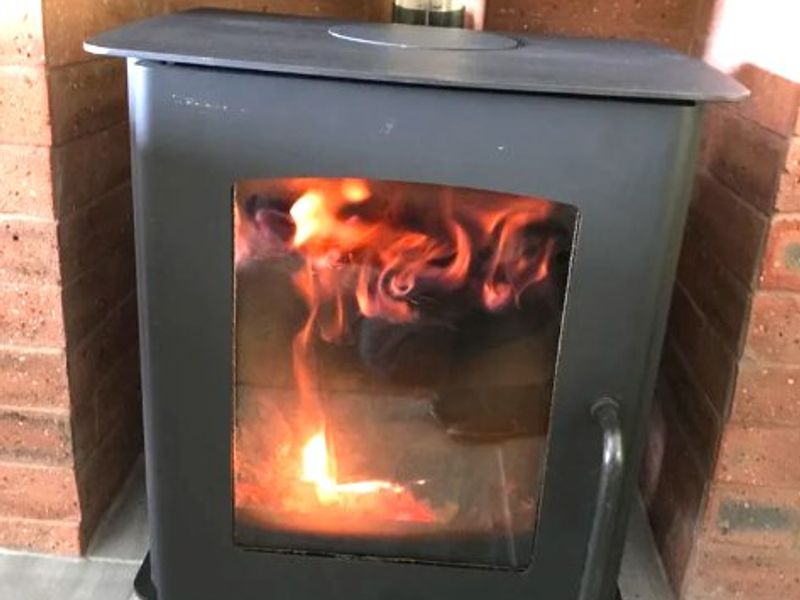 A modern black wood-burning stove set within a traditional brick fireplace surround and tiled hearth.