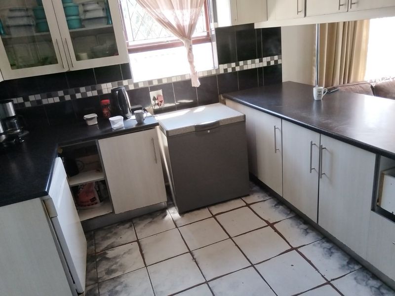 A functional kitchen featuring laminate cabinetry, dark countertops, and a tiled backsplash. The space requires some maintenance to the flooring and cabinetry.