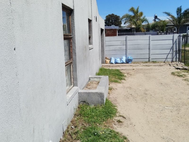 Rear exterior view of the property featuring a plastered wall, built-in concrete planter, and a precast concrete boundary wall with a metal gate.