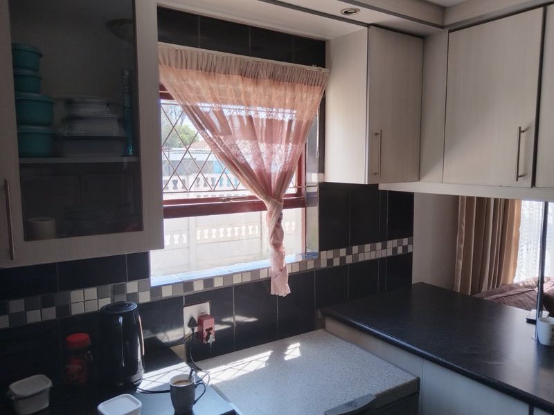 A functional kitchen area featuring built-in cabinetry, dark tiled backsplash, and laminate countertops with natural light from a window with security bars.