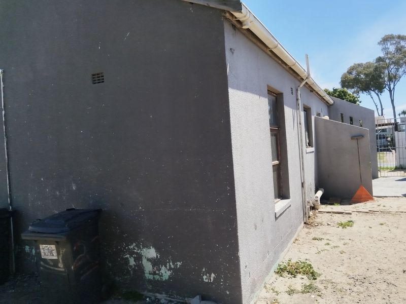 Rear exterior view of the property showing painted masonry walls, guttering, and downpipes, with visible signs of paint deterioration and weathering.