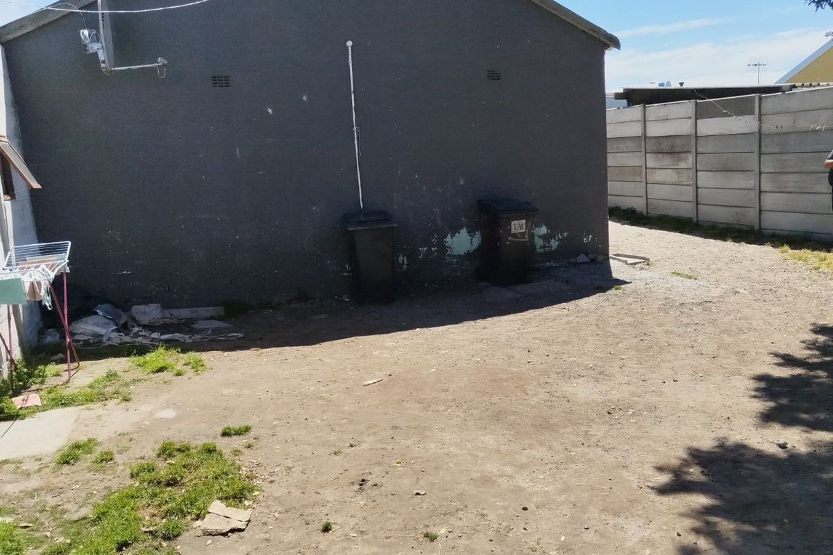 Rear exterior view of the property featuring a large unlandscaped yard area and a precast concrete boundary wall.