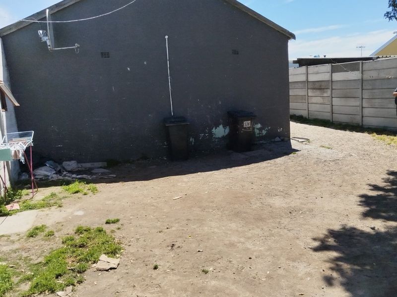 Rear exterior view of the property featuring a large unlandscaped yard area and a precast concrete boundary wall.