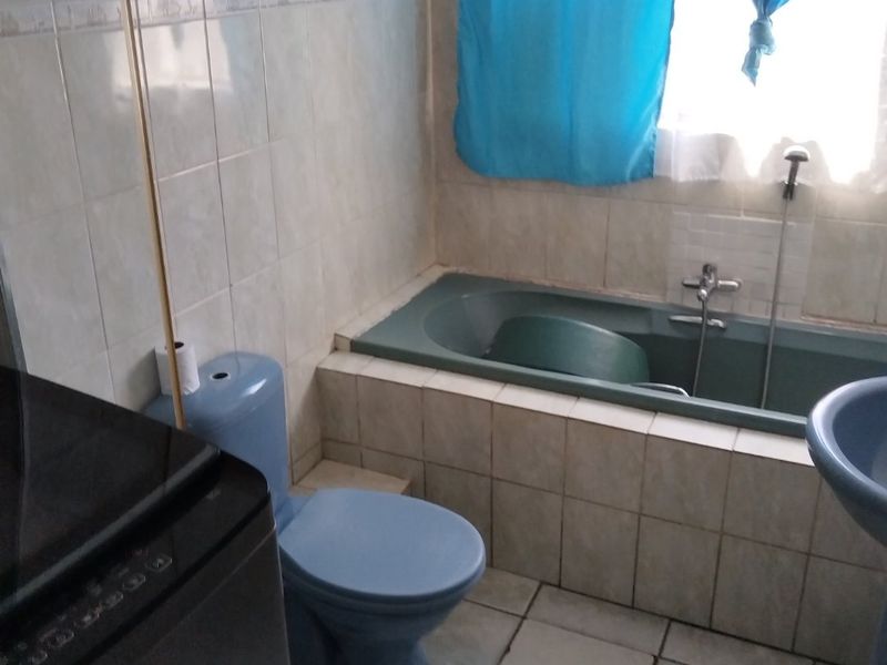 A dated bathroom featuring a built-in bathtub, blue toilet, and pedestal basin with tiled walls and flooring, requiring cosmetic updates.