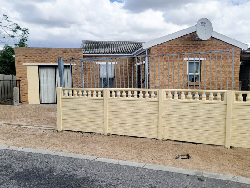 Front elevation of a face brick house featuring a precast boundary wall, steel security fencing, and a tiled roof.