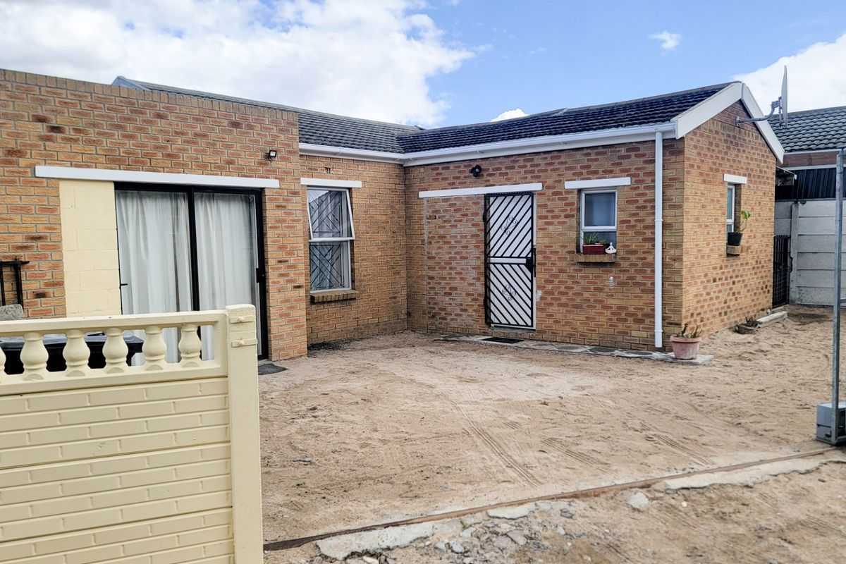 Rear view of a face brick house featuring a sliding door, security gate, and an unpaved yard area requiring landscaping.