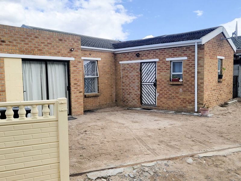 Rear view of a face brick house featuring a sliding door, security gate, and an unpaved yard area requiring landscaping.
