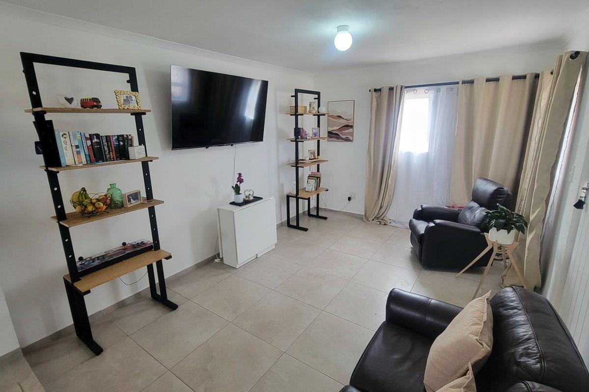 A bright living room featuring neutral tiled flooring, cove cornicing, and large windows with curtain rails, providing a clean and functional living space.