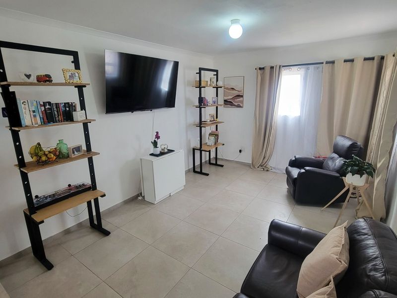 A bright living room featuring neutral tiled flooring, cove cornicing, and large windows with curtain rails, providing a clean and functional living space.