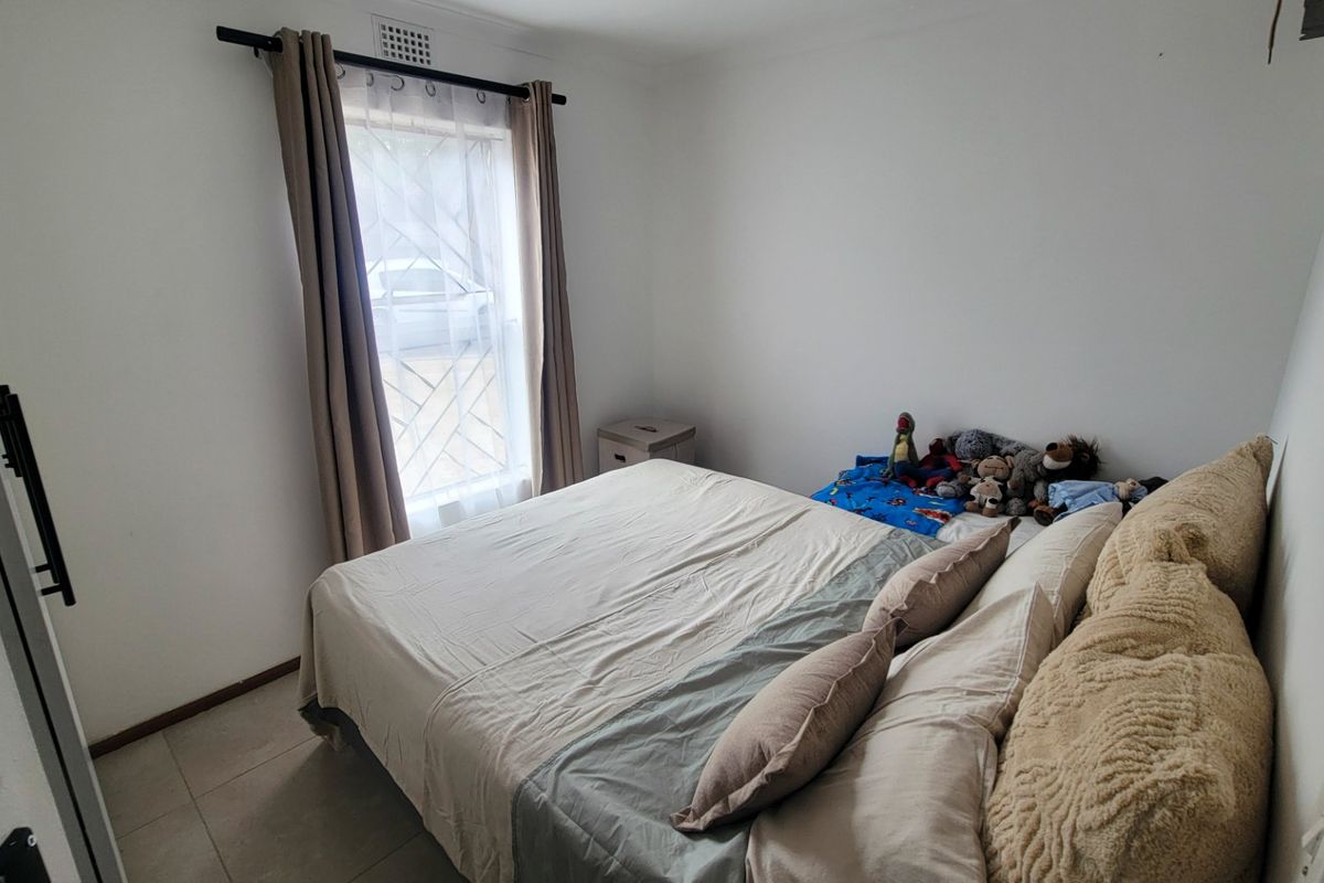 A standard bedroom featuring tiled flooring, a window with security bars, and neutral wall finishes.