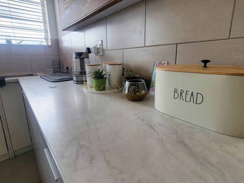 A functional kitchen area featuring a marble-effect countertop, tiled backsplash, and integrated sink with mixer tap, illuminated by natural light through venetian blinds.