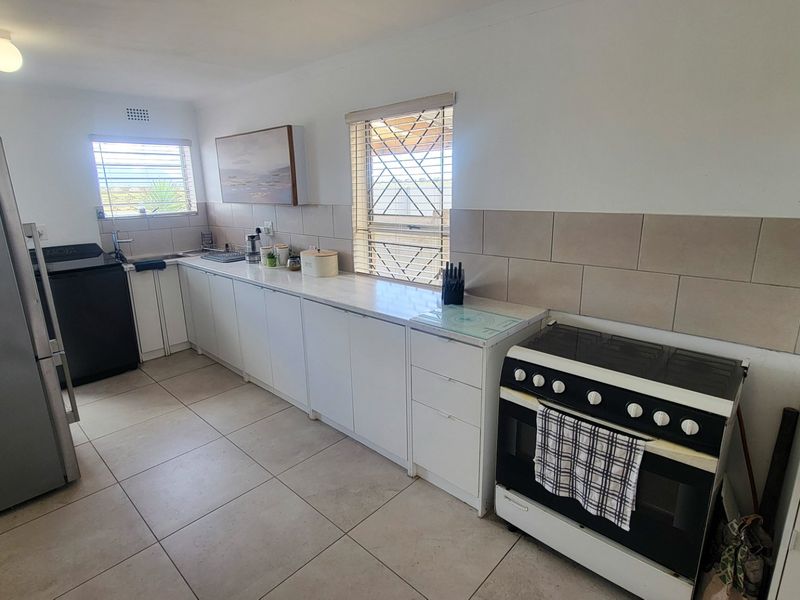 A functional kitchen featuring white cabinetry, tiled backsplash, tiled flooring, and a freestanding stove, with natural light provided by two windows.