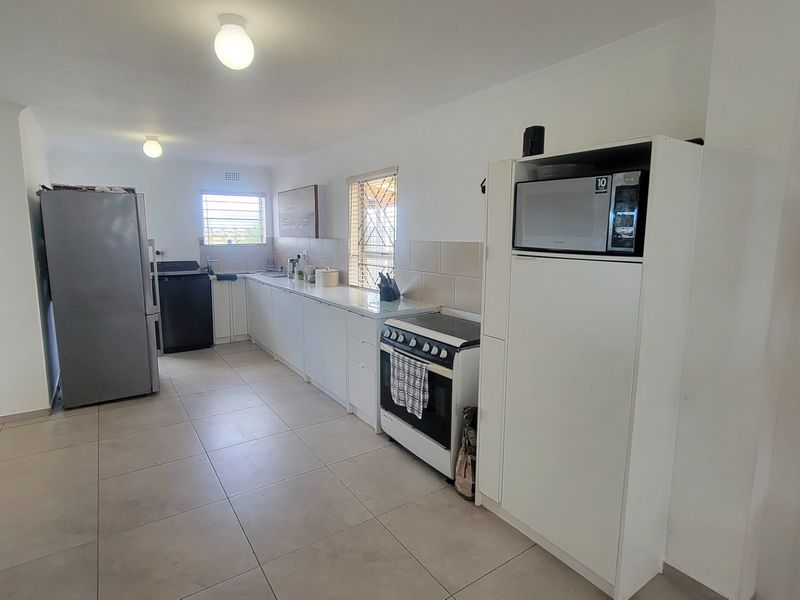 A functional kitchen featuring white cabinetry, tiled flooring, a tiled backsplash, and a freestanding stove with integrated microwave housing.