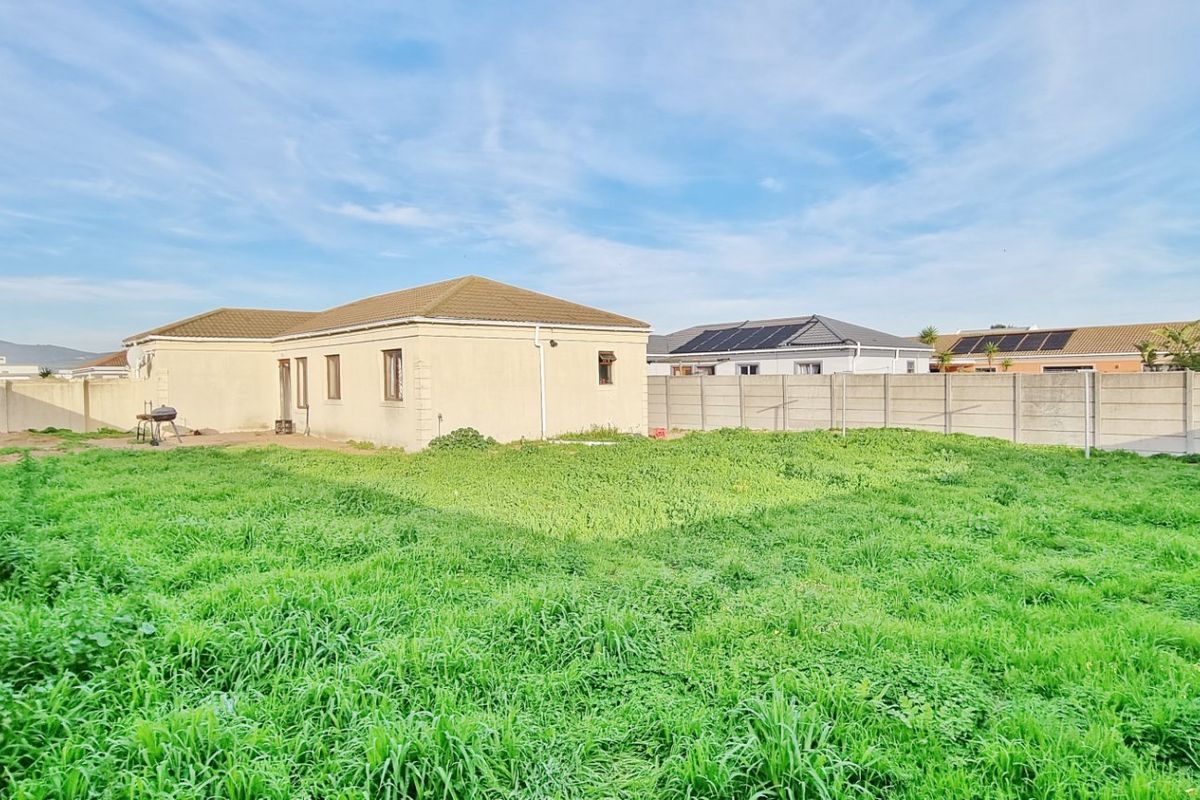 Spacious rear garden area featuring a large lawn, enclosed by precast concrete boundary walls, with a view of the rear building elevation.