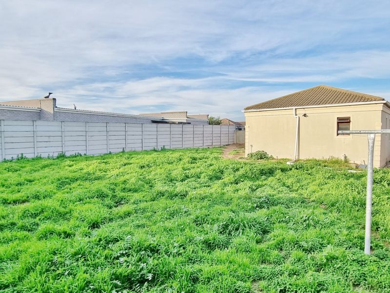A spacious rear garden area featuring a large lawn, enclosed by precast concrete boundary walls, with a view of the rear building elevation.