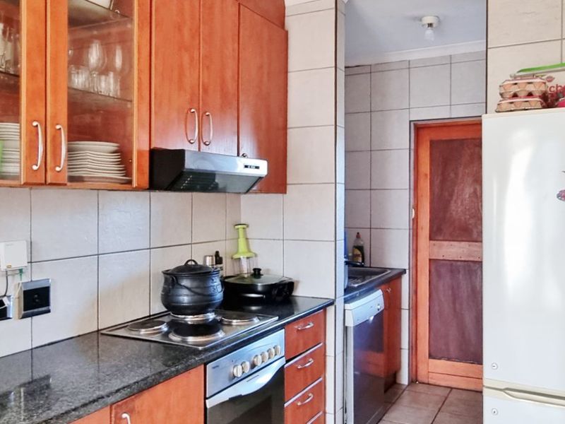 A functional kitchen featuring wooden cabinetry, granite countertops, a built-in oven with hob, and tiled finishes throughout.