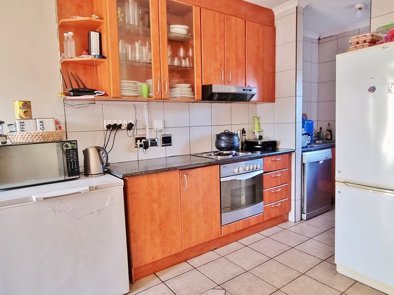 A functional kitchen featuring wooden cabinetry, granite countertops, built-in oven, and hob, with tiled flooring and a separate scullery area visible in the background.