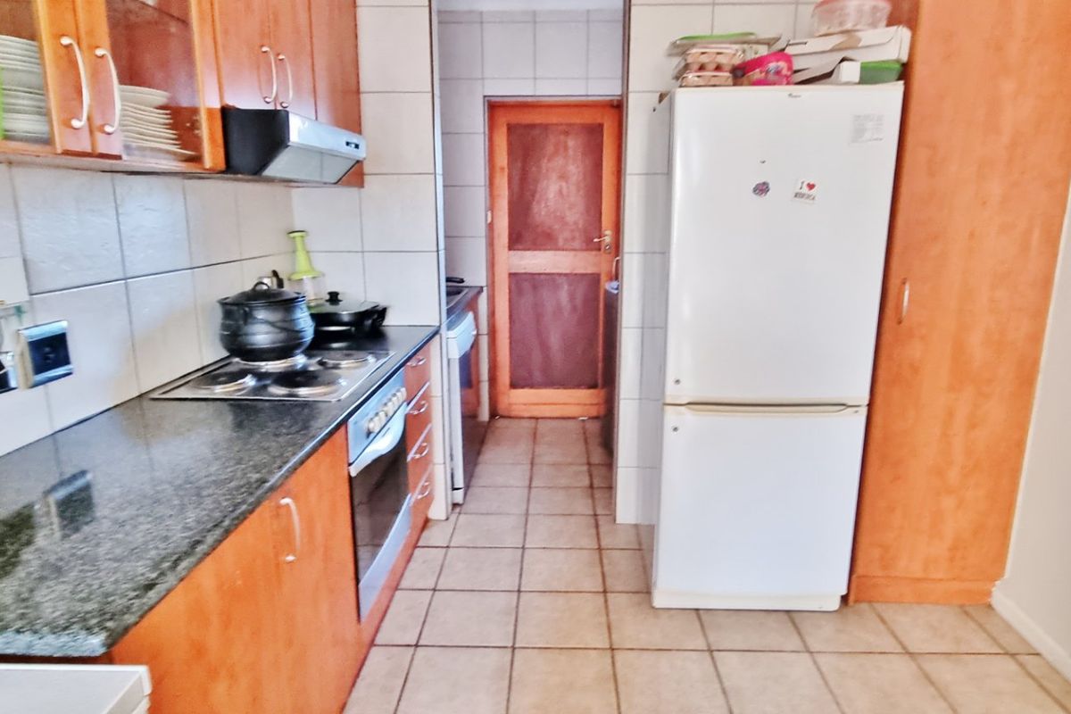 A functional kitchen featuring wooden cabinetry, granite countertops, built-in oven and hob, and tiled flooring with a separate pantry area.