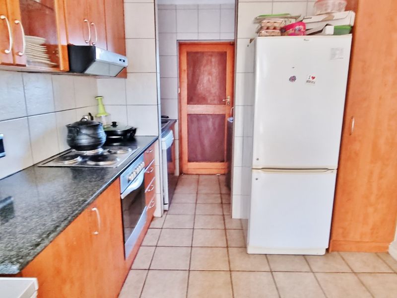 A functional kitchen featuring wooden cabinetry, granite countertops, built-in oven and hob, and tiled flooring with a separate pantry area.