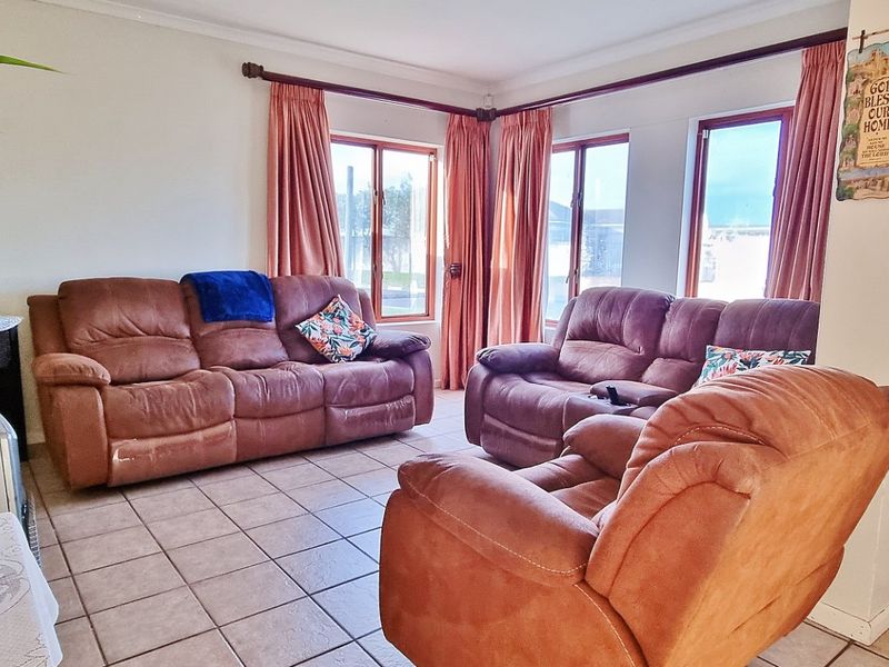 A living room featuring tiled flooring and large windows with timber frames, providing natural light to the space.