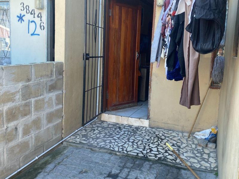 Front entrance area featuring a timber door with security gate, paved flooring, and masonry walling, showing signs of wear and requiring maintenance.