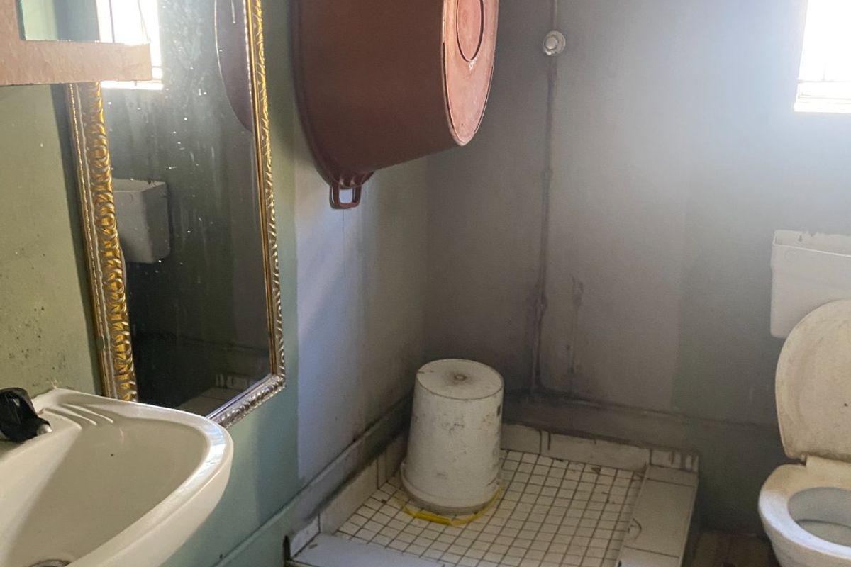 A small, dated bathroom featuring a pedestal basin, flush toilet, and a tiled shower base, currently requiring significant renovation and finish updates.