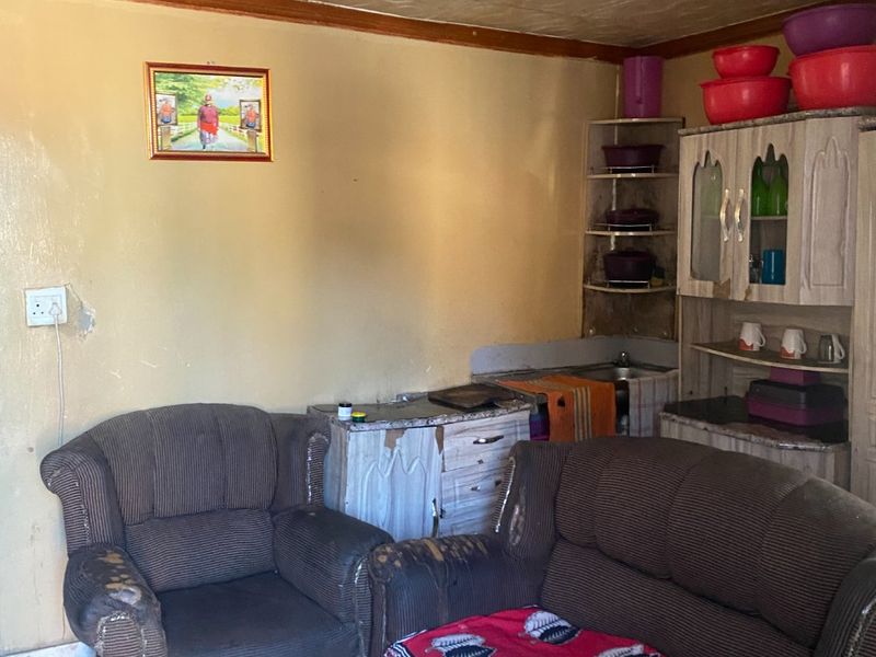 A compact kitchen area featuring built-in cabinetry, tiled flooring, and textured ceiling tiles, currently showing significant signs of wear and dated finishes.