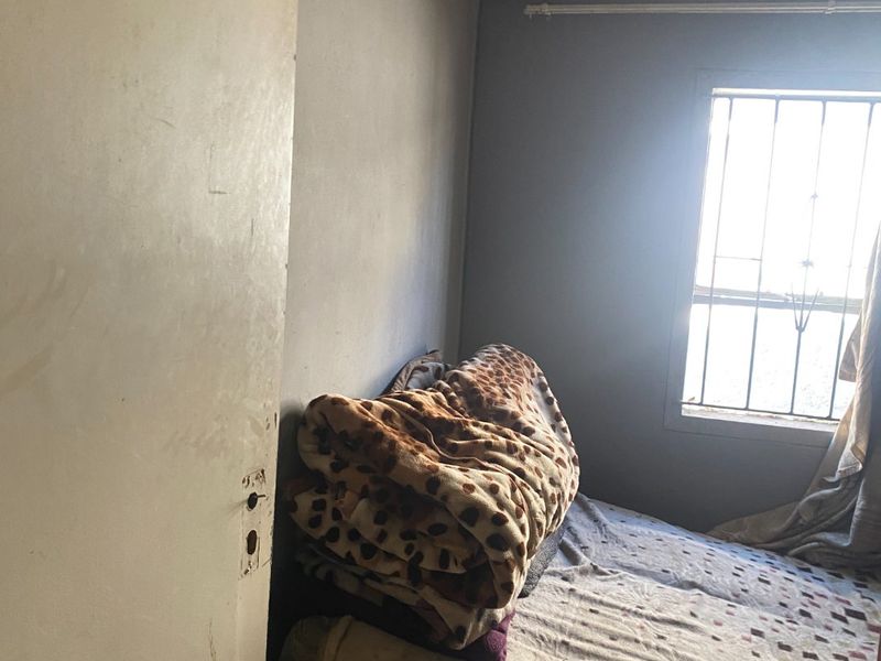 A bedroom featuring decorative ceiling tiles and a window with security bars, requiring cosmetic updates to improve the overall condition.
