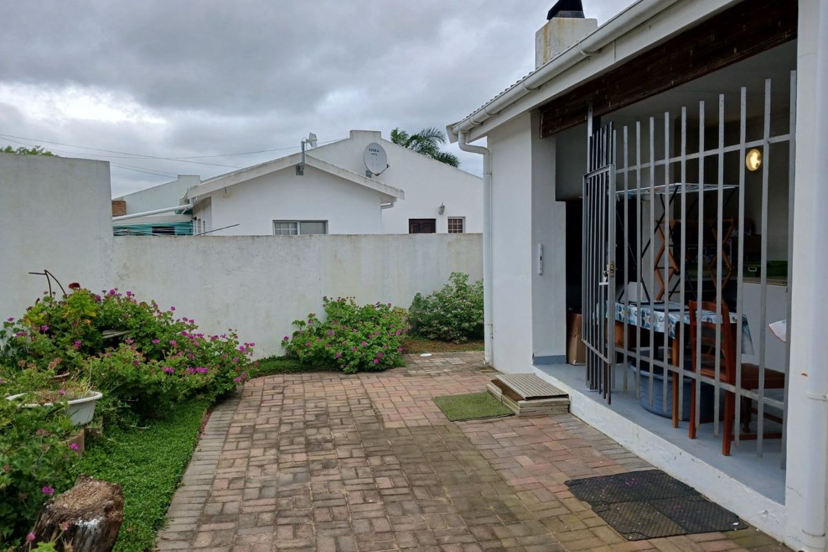 A rear exterior view featuring a paved patio area, a security gate leading to the home, and a boundary wall.