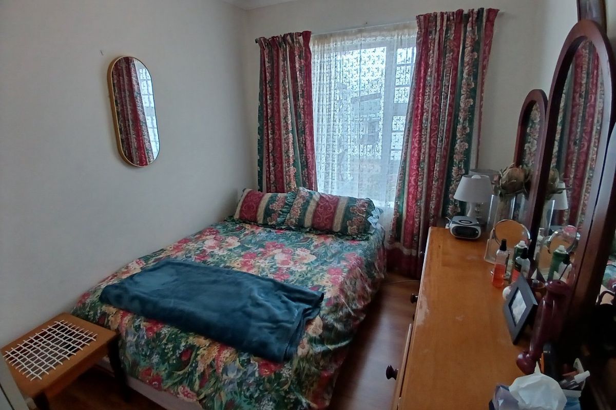 A compact bedroom featuring laminate flooring and a window with curtains, offering a functional space for rest.