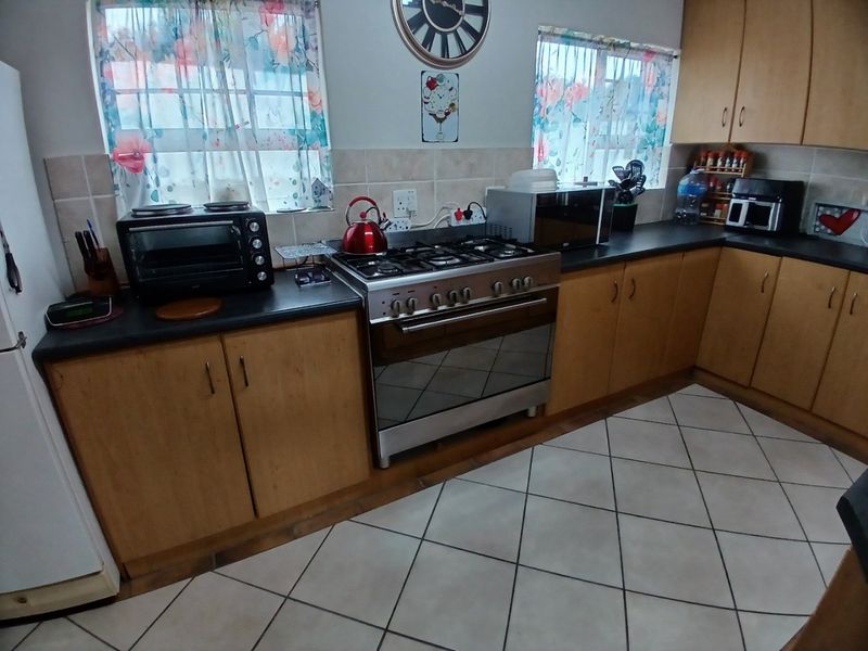 A functional kitchen featuring wooden cabinetry, a gas stove with oven, tiled backsplash, and tiled flooring.