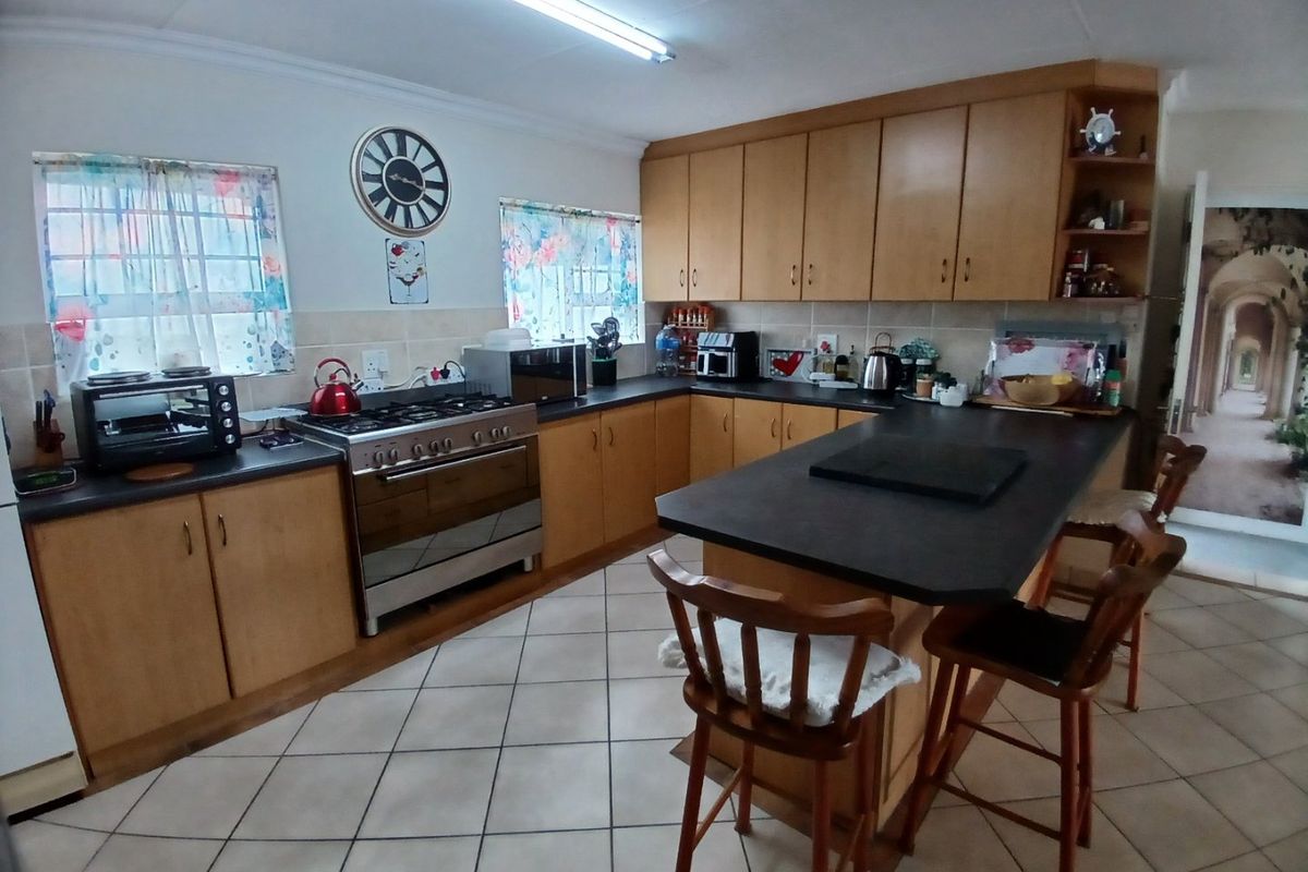 A functional kitchen featuring wooden cabinetry, dark laminate countertops, a gas stove, and a central island with tiled flooring throughout.