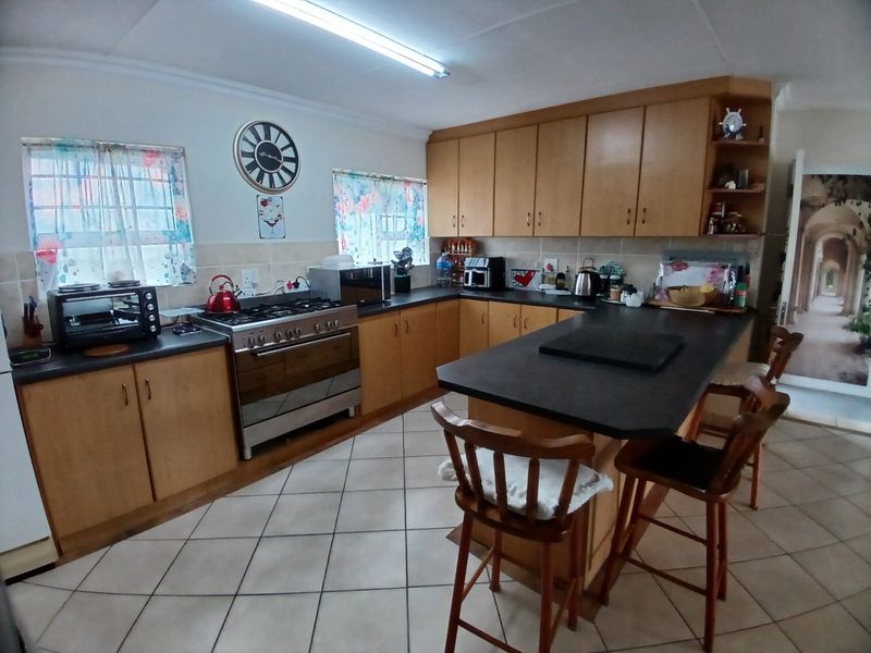 A functional kitchen featuring wooden cabinetry, dark laminate countertops, a gas stove, and a central island with tiled flooring throughout.