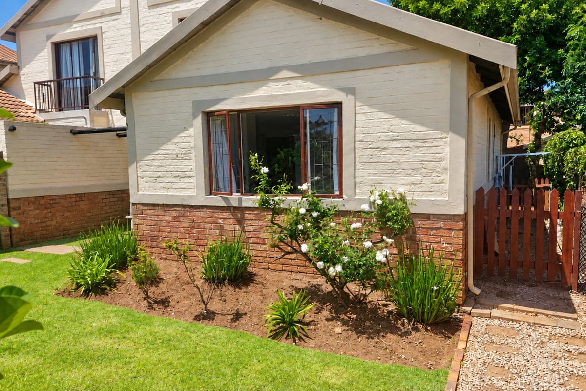 Rear view of the townhouse featuring a brick and painted facade, casement windows, a small garden, and a timber gate leading to a gravel path.