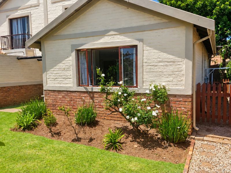 Rear view of the townhouse featuring a brick and painted facade, casement windows, a small garden, and a timber gate leading to a gravel path.