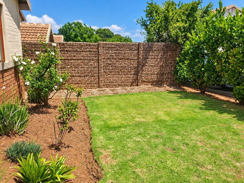 A private rear garden featuring a well-maintained lawn, landscaped garden beds, and a secure precast concrete boundary wall.
