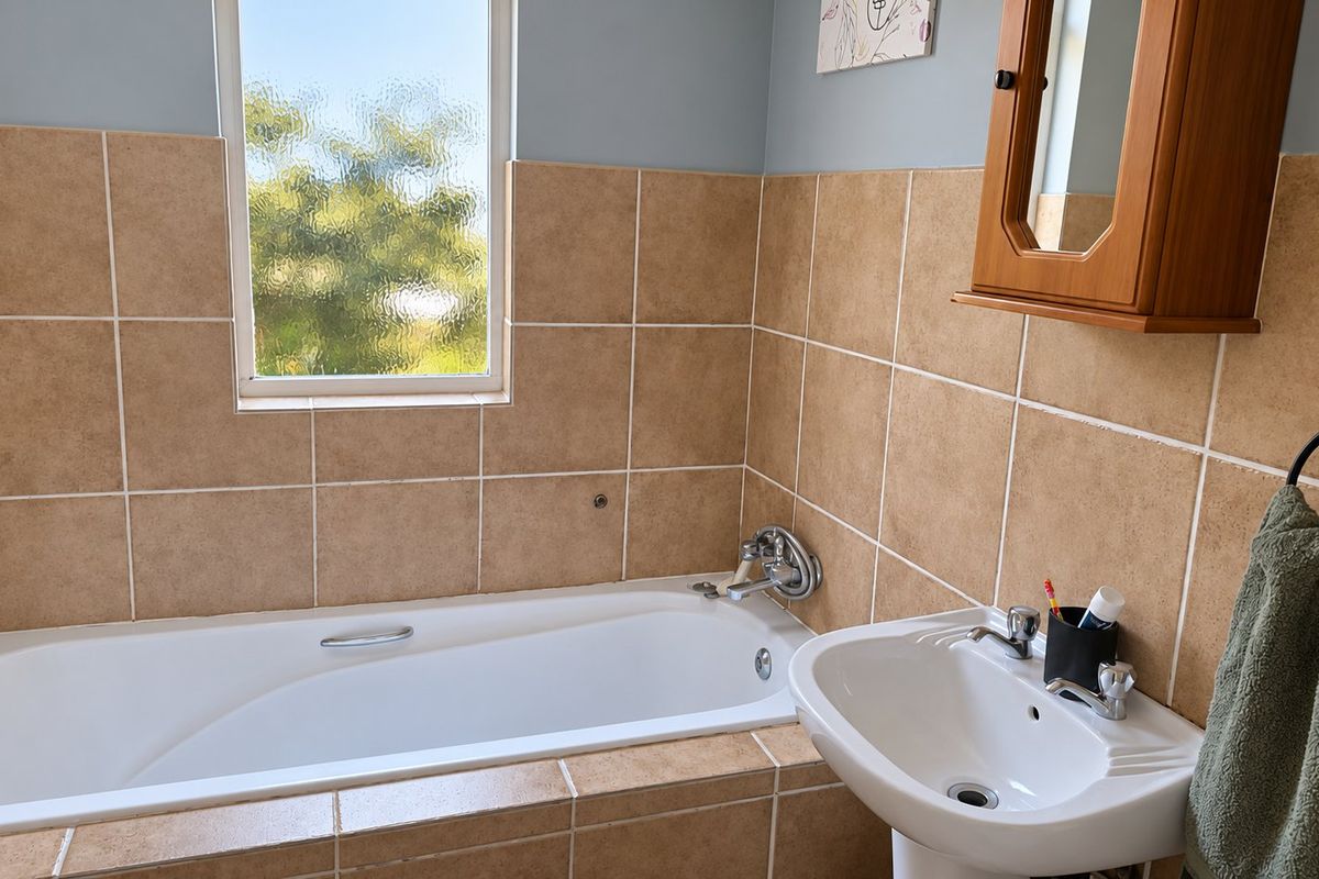 A functional bathroom featuring a bathtub with tiled surround, a pedestal basin, and a wall-mounted medicine cabinet with natural light from the window.