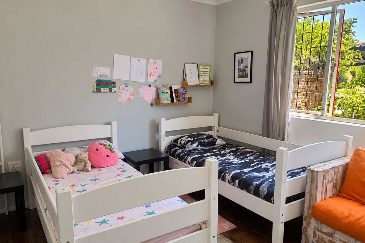 A functional bedroom featuring laminate flooring and a window with security bars, providing natural light and a view of the garden area.
