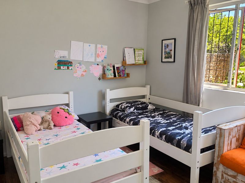 A functional bedroom featuring laminate flooring and a window with security bars, providing natural light and a view of the garden area.