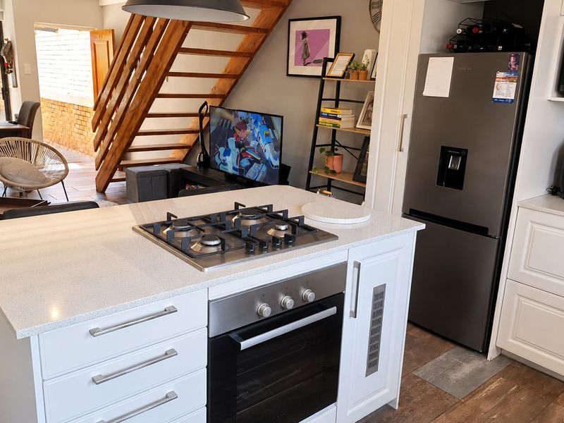 Open plan kitchen featuring a central island with gas hob and oven, white cabinetry, stone countertops, and a wooden staircase leading to the upper level.