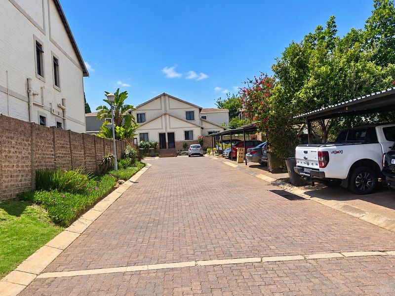 A view of the townhouse complex driveway featuring paved surfaces, covered parking bays, and established boundary walls with garden landscaping.