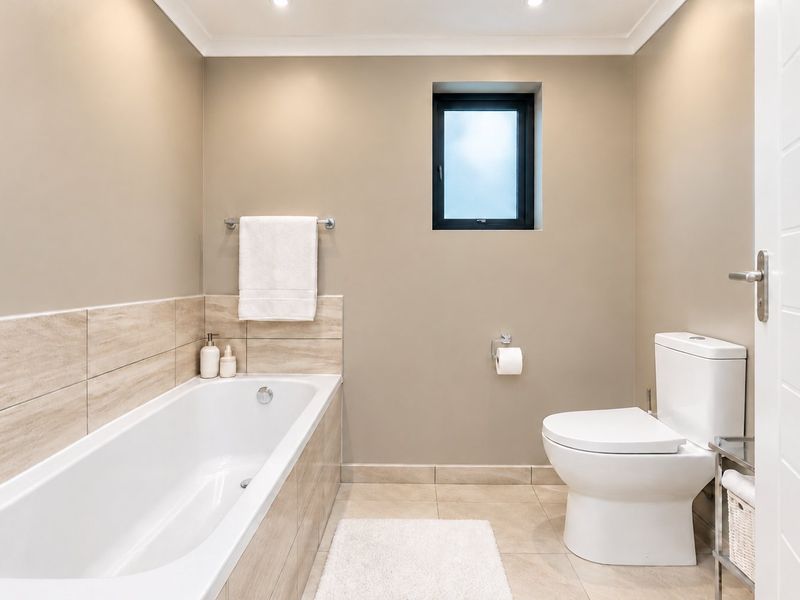 A clean and modern bathroom featuring a built-in bathtub with tiled surround, a toilet, and neutral wall finishes with recessed lighting.
