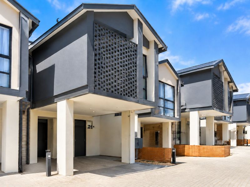 Modern townhouse exterior featuring a paved driveway, covered parking, and contemporary architectural details including decorative screening and timber accents.