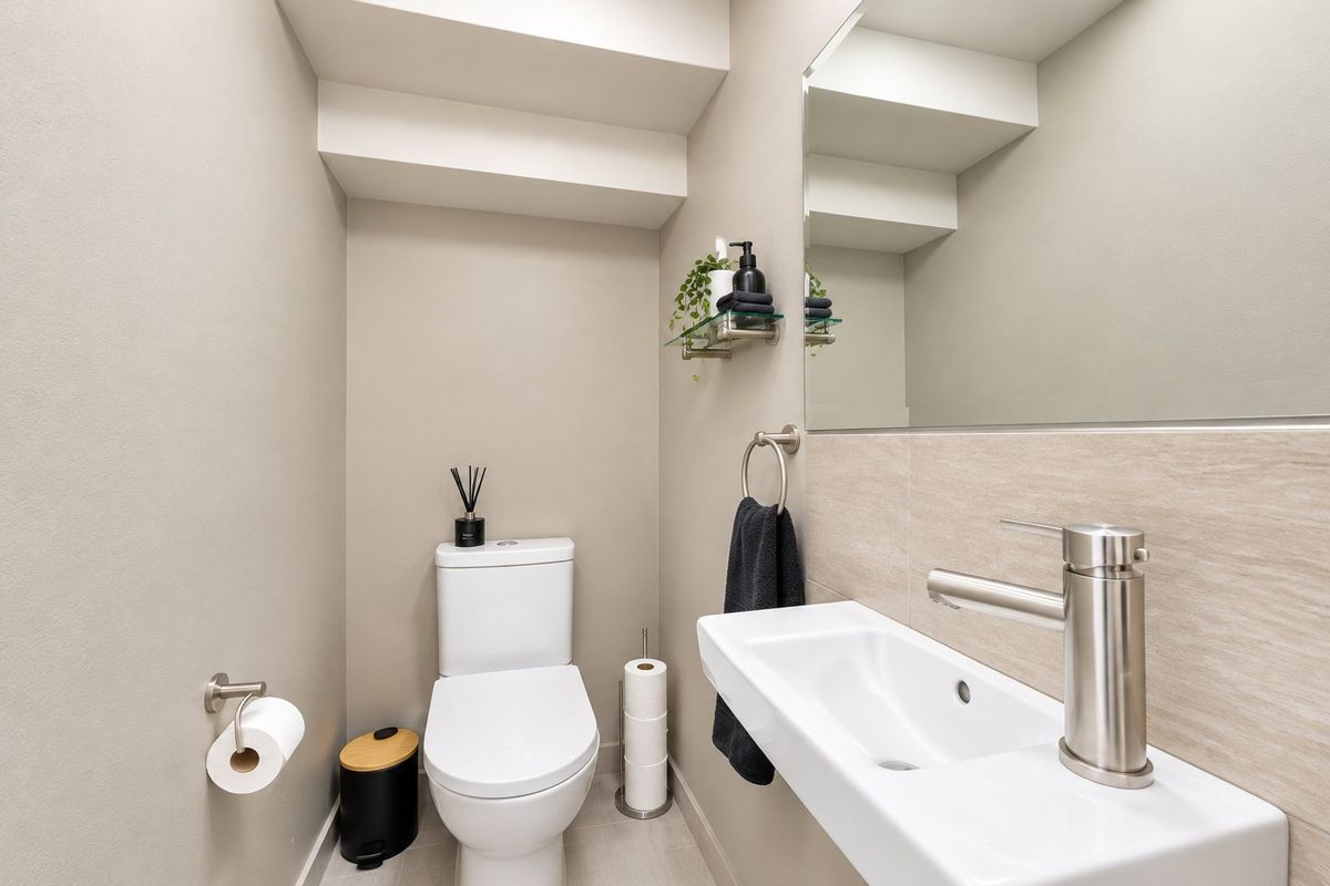 A modern, well-maintained powder room featuring a wall-mounted basin, contemporary faucet, dual-flush toilet, and a large mirror with neutral tiling.