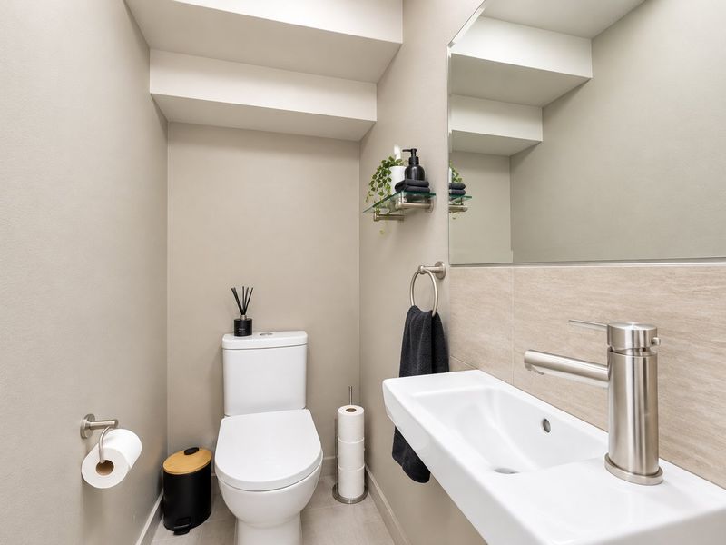 A modern, well-maintained powder room featuring a wall-mounted basin, contemporary faucet, dual-flush toilet, and a large mirror with neutral tiling.
