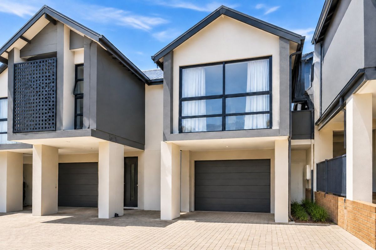 Modern townhouse exterior featuring a paved driveway, double garage, and contemporary architectural design with clean lines and large windows.