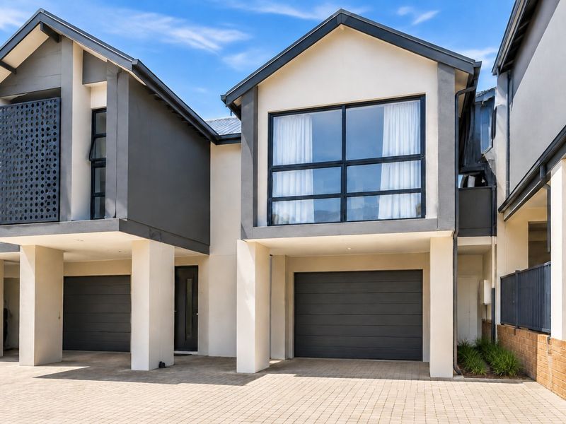 Modern townhouse exterior featuring a paved driveway, double garage, and contemporary architectural design with clean lines and large windows.