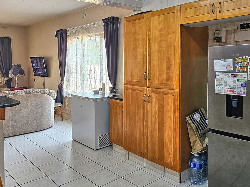 Open plan living and kitchen area featuring wooden cabinetry, tiled flooring, and a breakfast counter, offering a functional and connected living space.