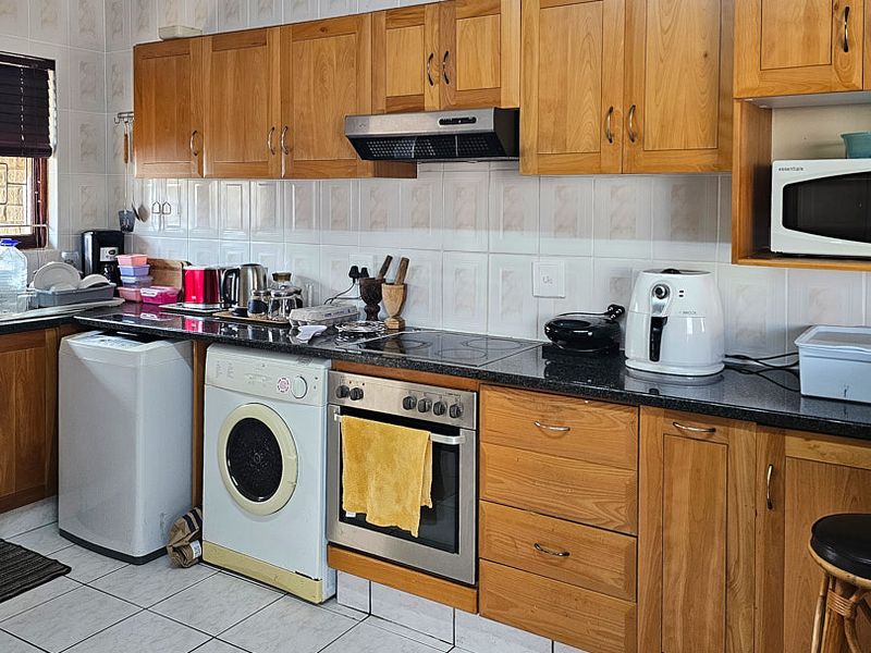 A functional kitchen featuring wooden cabinetry, granite countertops, a built-in oven with hob, and integrated laundry appliance space.